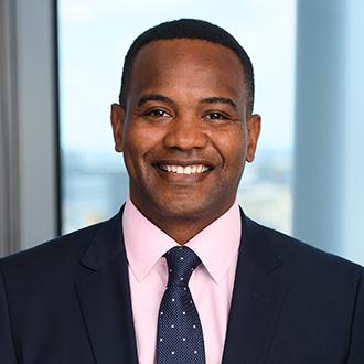 Man smiling wearing black jacket, light pink shirt and blue navy tie